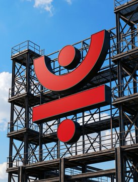 A large red JustLend DAO “J” logo stands against a steel framework and blue sky. The image visually represents JustLend DAO and its sTRX staking product, whose returns are tied to the network’s underlying utility and revenue-generating activities.