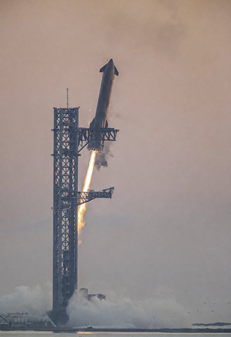 A SpaceX Starship rocket lifts off from its launch tower with bright orange flames and billowing smoke, ascending into a hazy sky — visually embodying the post's message that this scene will soon become a routine reality.