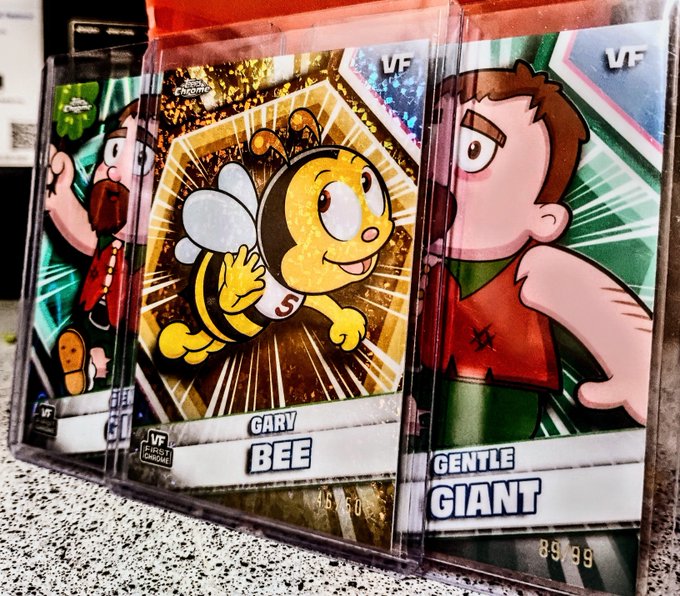 Three cartoon trading cards displayed at a counter, featuring 'GARY BEE' and 'GENTLE GIANT' with VF condition ratings and prices like 85/50 and 85/99.