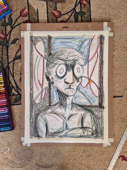 A hand-drawn colored pencil sketch of a wide-eyed, bald humanoid figure with large butterfly-like wings, taped to a board on a patterned carpet next to a set of colored pencils and a ruler.