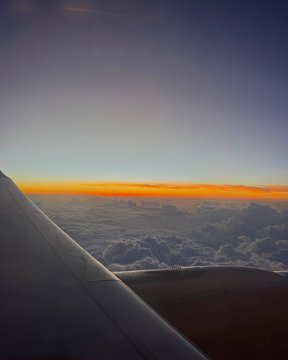 A view from an airplane window showing the wing above a layer of clouds at sunset with an orange and purple sky.