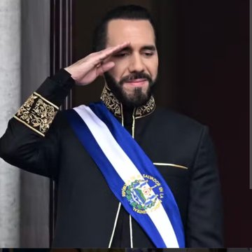 A man with a beard, wearing a black military-style uniform with gold embroidered shoulder details and a blue-and-white presidential sash bearing the El Salvador coat of arms, stands at attention while saluting with his right hand. The image appears to show El Salvador's President Nayib Bukele, relating to the news about his government's recent licensing of Modveon's "Sivar" national payment app.