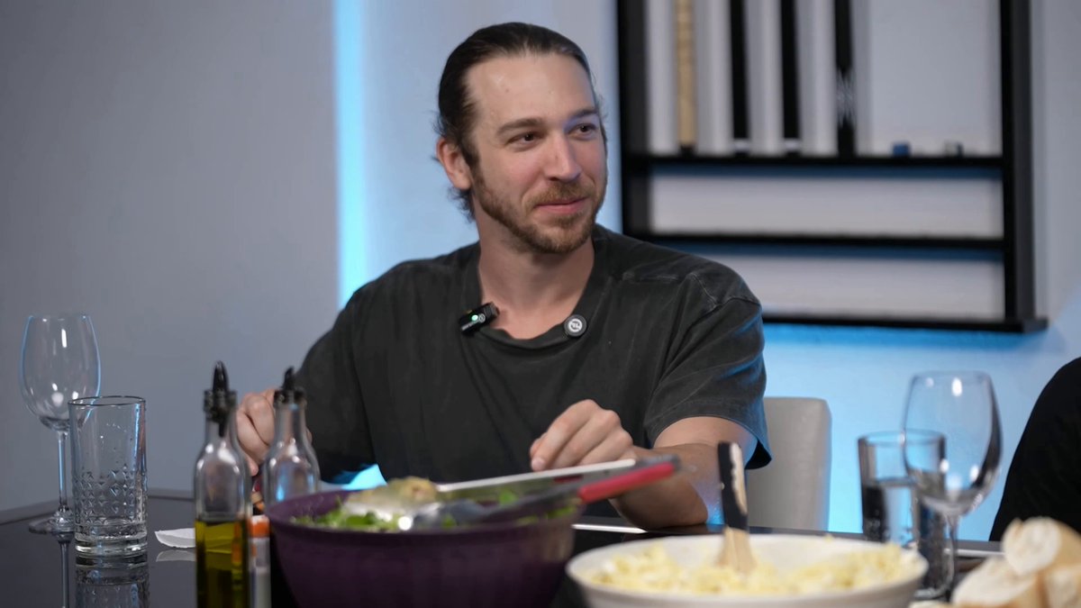 The image shows a man sitting at a dining table with various items such as wine glasses, bowls of food, and bottles. The man appears to be eating or preparing his meal while seated at the table. The scene also includes a caption that reads "Wall Street institutions care about decentralization Etherealize co-founder and a key architect behind Ethereum's transition to proof-of-stake".