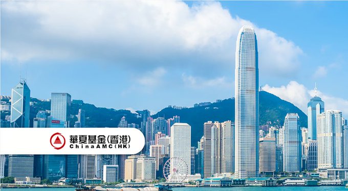 A panoramic view of Hong Kong's skyline featuring the IFC Tower and Central district along the harbor, with the ChinaAMC (Hong Kong) "華夏基金（香港）" logo overlaid in the lower-left corner, illustrating the company's role in completing the city's first stablecoin purchase of a tokenized fund in partnership with Standard Chartered and OSL.