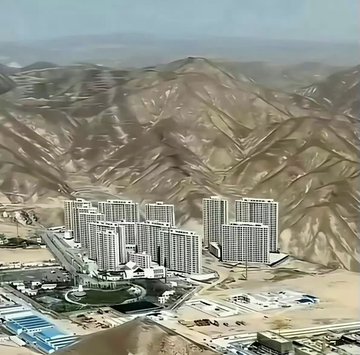 An aerial view of a large modern residential development with multiple high-rise apartment buildings situated in an arid, mountainous region.