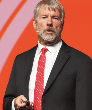 Michael Saylor, executive chairman of Strategy (formerly MicroStrategy), is shown on stage speaking, likely at a Bitcoin or cryptocurrency conference, in an image relevant to the news about his company's recent $263.5 million stock sale used to boost its USD reserves rather than purchase additional Bitcoin.