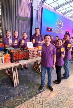 A group of people in purple Pi Network shirts standing together at a Pi Network event with crates of oranges.
