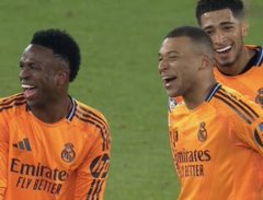 Three Real Madrid soccer players in orange "Emirates FLY BETTER" jerseys celebrate joyfully on the pitch.