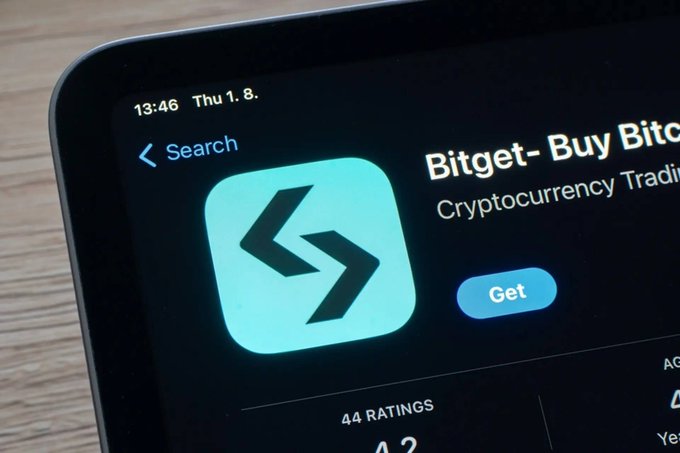 A close-up of a smartphone screen displays the Bitget app on the App Store with the text "Bitget - Buy Bitcoin" and "Cryptocurrency Trading," along with a "Get" button and "44 RATINGS" visible.