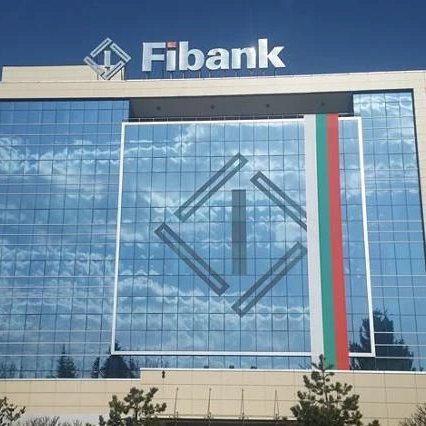 The image shows the modern glass facade of Fibank's headquarters, prominently displaying the bank's logo and name at the top alongside the Bulgarian flag colors—visually identifying the institution mentioned in the news that Bulgaria's First Investment Bank (Fibank) is launching crypto investing services to its over 1 million customers.