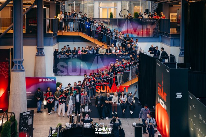 A large group of people gathers at the Solana Summit event, posing on multi-level staircases with 'SOLANA SUMMIT' branding visible.