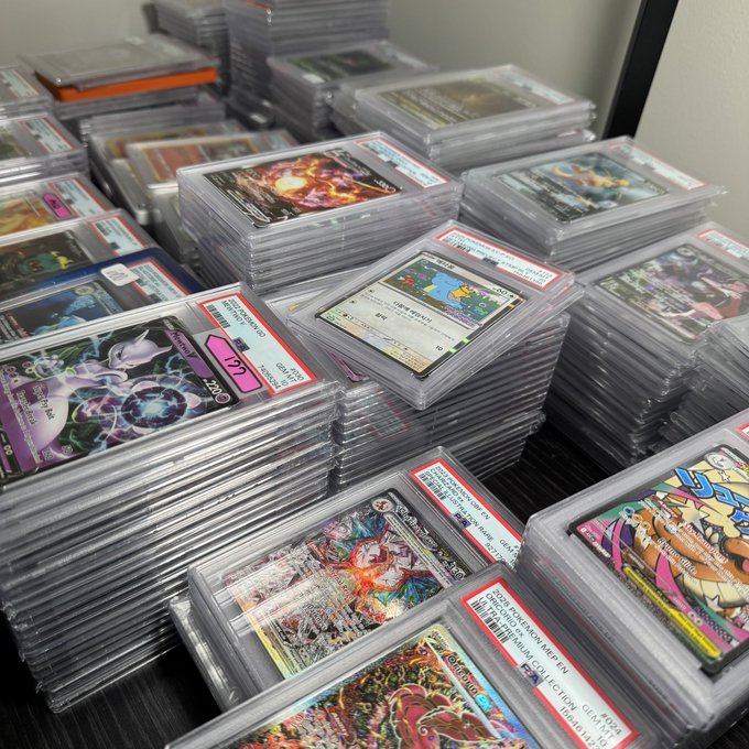 Stacks of graded Pokémon cards in PSA slabs, including notable cards like "Lugia V" (PSA 10) and "Pikachu VMAX," are piled on a desk for the @BONKUJI_inu gacha event. The labeled slabs and high-grade cards reflect the collection being added to the gacha pool.