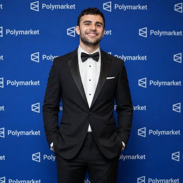 A man in a black tuxedo with a bow tie smiles while standing in front of a blue backdrop branded with the "Polymarket" logo.