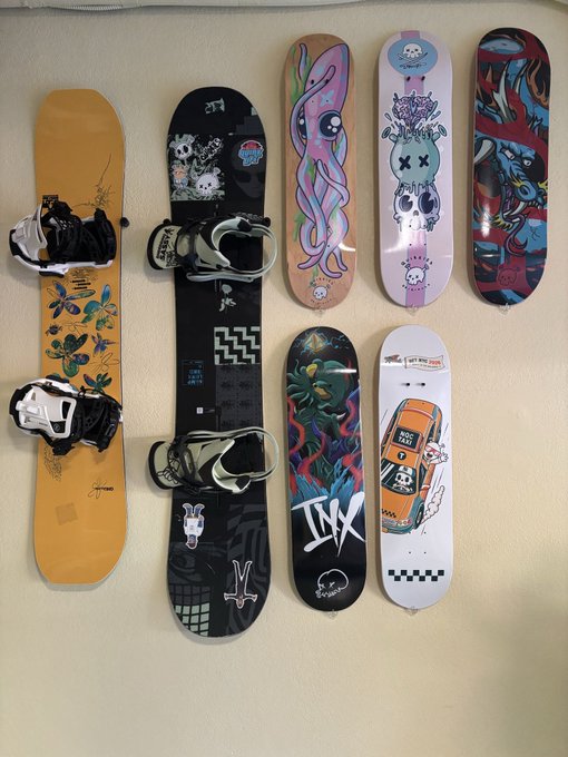 A collection of snowboards and skate decks displayed on a wall, featuring colorful graphics including octopuses, characters, and car illustrations.