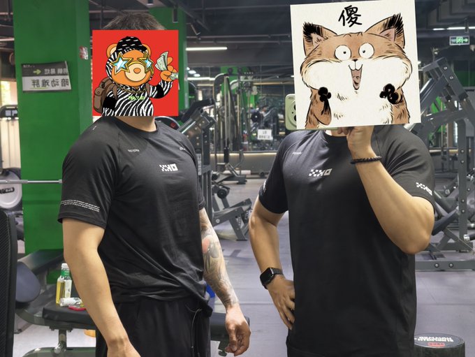 Two men in black athletic shirts pose in a gym, with their faces covered by cartoon stickers - one with a character in a striped shirt and the other a shocked-looking cat with the Chinese character '傻'.