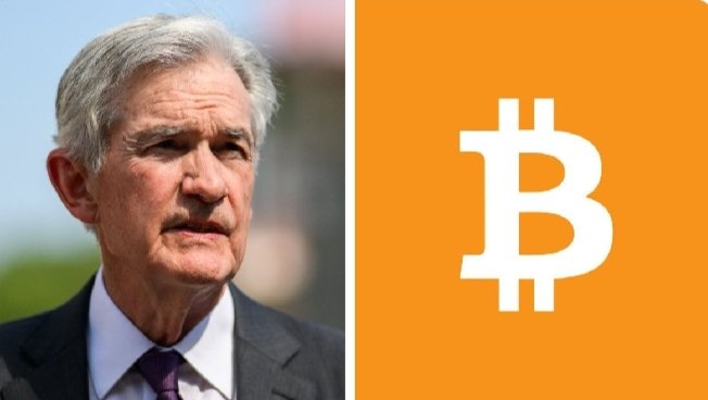 The image features an older man wearing a suit, standing next to a large orange square containing the letter "B" inside of it. The man appears to be looking off into the distance or at something outside the frame. The background of the image is white with some text visible on it that reads "Federal Reserve Chair Jerome Powell once again compared Bitcoin to gold". This text suggests that the man's comparison of Bitcoin to gold might have been made by someone else, possibly a financial expert or an article discussing the value of Bitcoin in relation to traditional assets like gold.