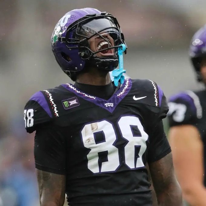 A football player wearing a black and purple TCU uniform with the number 88, shouting in the rain with a blue mouthguard hanging from his facemask.