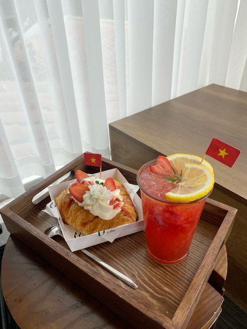 A wooden tray holds a strawberry-topped croissant and a red strawberry-lemon drink, both decorated with small Vietnamese flags. While the post discusses crypto topics like RWAs and TradFi, the image itself simply showcases an aesthetically pleasing breakfast setup with no visible connection to the financial commentary.