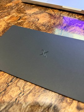 A dark gray card with a subtle "X" logo is shown, likely the @XMoney Card mentioned in the accompanying post, suggesting perfect timing for its use or arrival.
