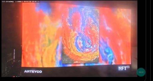 A screen displays a colorful abstract digital artwork from 'ARTEYCO' alongside an 'NFT' logo, captured as a photo of a monitor.
