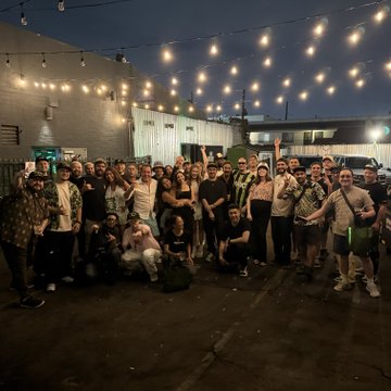 A large group of people poses together outdoors at night under string lights, celebrating what appears to be a casual social gathering.