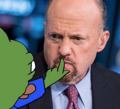 A crude green cartoon character reaches toward the nose of a man in a suit and tie, who has a skeptical expression in what appears to be a news interview setting.