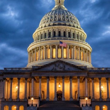 A photograph of the United States Capitol building dome illuminated at dusk with an American flag flying.