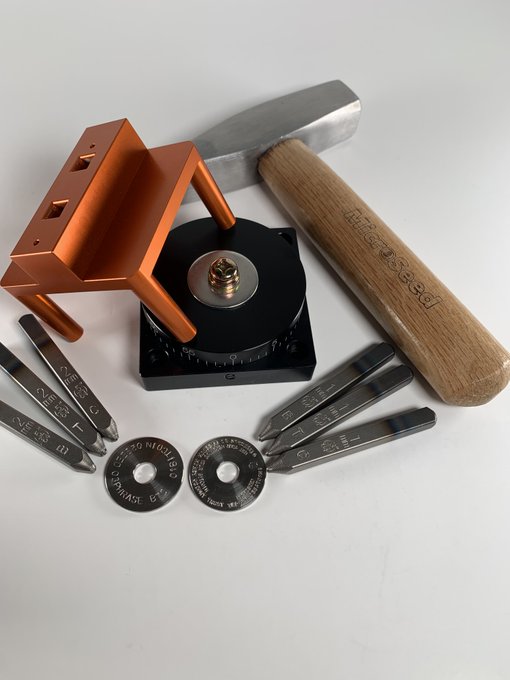 A copper MicroSeed punch tool sits alongside its steel "BITCOIN" branded hammer, center punch, and several metal washers engraved with "MICROSEED," "DO NOT SPIN," and "IN GOD WE TRUST" ready to stamp Bitcoin seed phrases onto washers as a durable backup solution.