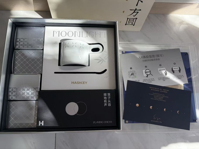 An opened product box displays a 'MOONLIGHT HASHKEY' wallet device alongside instruction cards and a charging cable, with Chinese text including '落子从容 掷地有声' and 'PLAYING CHESS' visible on the packaging.