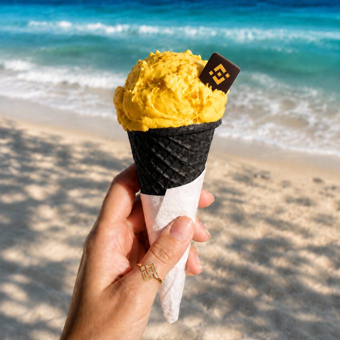 A hand holds a black waffle cone filled with bright yellow ice cream, garnished with a small chocolate piece bearing a logo, set against a sunny beach backdrop. The post "GM今日份甜度：七夕限定" (Good morning, today's sweetness: Qixi limited edition) ties the image to a romantic Qixi Festival treat, blending the cheerful yellow dessert and seaside setting as a sweet summer greeting.