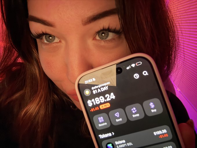 A woman holds her phone up to the camera, showing a crypto portfolio app displaying a total of $189.24 with a +$1.45 (0.76%) gain, with Solana (SOL) listed at the bottom—visually documenting her $1 daily accumulation challenge.