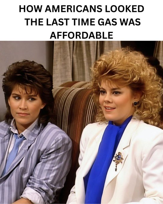 The image features two women sitting together, both wearing business attire with striped blazers. One of them has blonde hair styled in a curly manner, while the other woman has straight hair. The background includes a couch and curtains, creating an indoor setting for their conversation or gathering.