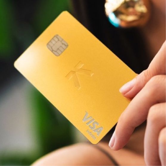 A person holds a gold Visa Infinite credit card with an embedded chip, featuring a stylized 'K' or asterisk-like logo.