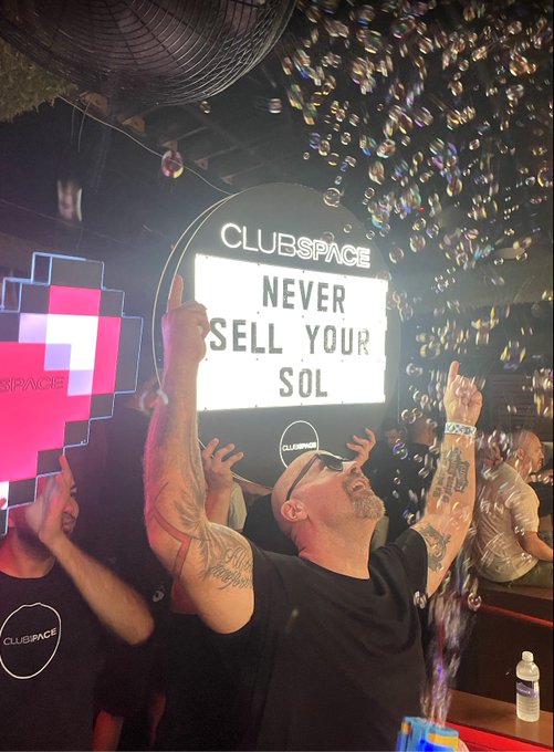 A man celebrates amid a cascade of bubbles at Club Space, with an illuminated sign behind him reading "CLUBSPACE NEVER SELL YOUR SOL," reinforcing the post's bullish message on $SOL.