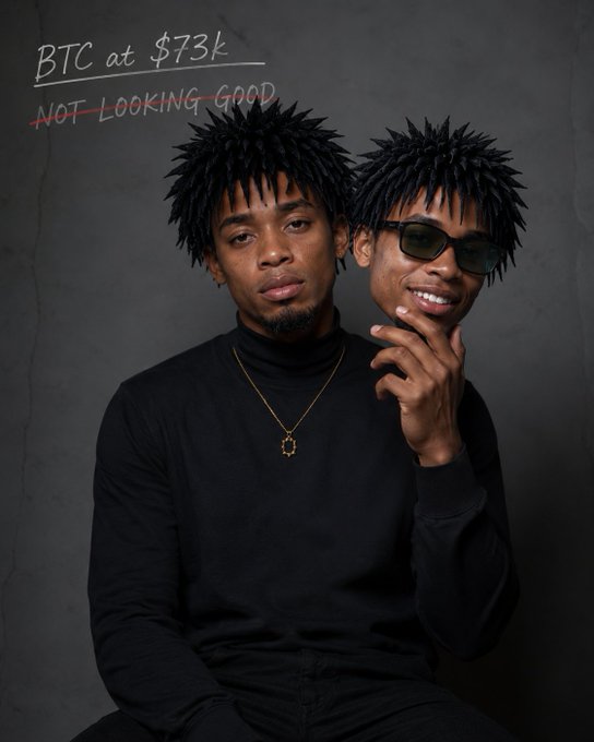 The image features two men wearing black clothing, with one man's face partially obscured by another man's head. The man whose face is hidden has spiky hair and sunglasses, while the other man wears a necklace around his neck. They are both sitting in front of a gray wall, which serves as the backdrop for their photo.

The image also contains text that reads "gm to everyone waking up to Bitcoin this low makes me want to go back to sleep I feel the bottom is almost be in and can't wait to open a fat long on @useTria". This message seems to be related to the content of the post, as it appears to be discussing Bitcoin or cryptocurrency.