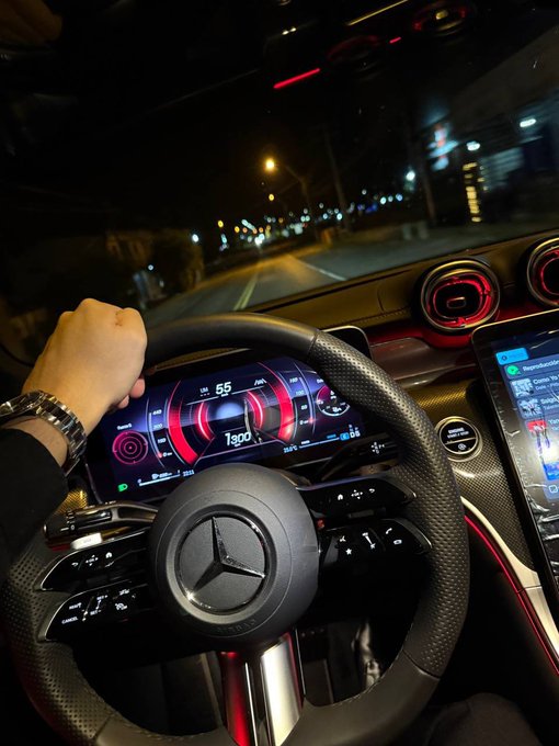 A nighttime drive captured from behind the wheel of a Mercedes, with the digital dashboard showing a speed of 55 mph, RPM of 1300, and ambient red cabin lighting—evoking a sense of forward motion and progress, fitting the post's theme of QuipNetwork and TheARCTERMINAL pushing blockchain innovation into the future.