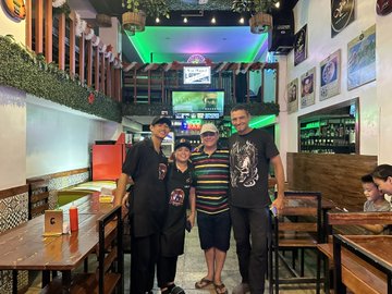 The image shows four people posing for a photo at a restaurant, with two men wearing black shirts and one man wearing a doginal dogs t-shirt. The group appears to be enjoying their time together as they stand close to each other, capturing a moment in their lives. In the background, there is a TV screen mounted on the wall above them, which might be displaying information about the restaurant or playing some entertainment for the guests.

The post includes text that reads "This is me before and after I became a @doginaldogs !!! Let me see yours Before. After". This suggests that the group's photo was taken during their time at the restaurant, possibly as part of a celebration or special occasion related to the doginal dogs theme.