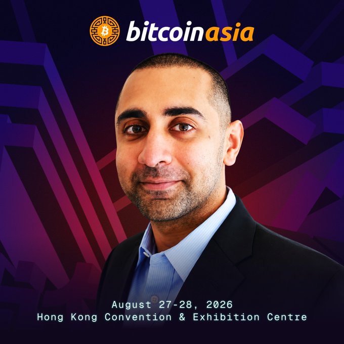 The image features a man wearing a suit and tie with a bald head and short hair. He has a smile on his face as he looks directly at the camera. The background of the image is dark, which contrasts with the bright colors used for the text in the image. The text reads "BITCOINASIA", indicating that this photo was taken at an event related to Bitcoin or cryptocurrency. The date and time are also included in the image.