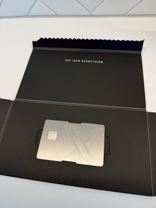A sleek metallic "X" branded credit card is displayed in its black packaging, which reads "TAP INTO EVERYTHING" — fitting promotional material for the launch of X Money, the new payment service from X (formerly Twitter).