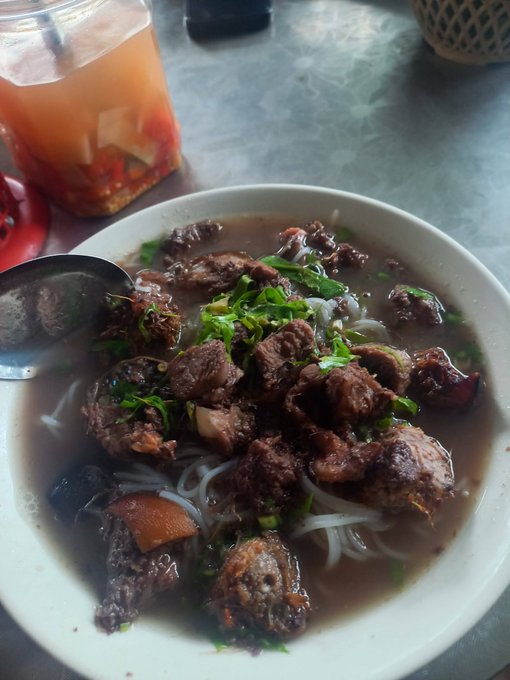 A steaming bowl of beef pho with rice noodles, tender chunks of meat, and fresh herbs, served alongside a jar of chili sauce on a metal table. The hearty breakfast pairs nicely with the post's encouraging message about starting each day with nourishing simplicity and steady progress—one step at a time.
