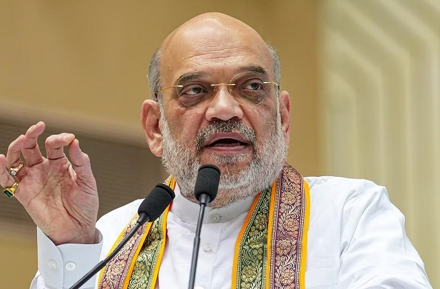 Amit Shah, India's Home Minister, speaks animatedly at a podium while wearing traditional attire with a saffron, gold, and green scarf, delivering remarks about the establishment of a Darknet Crypto Cell to track cryptocurrency payments tied to drug networks.