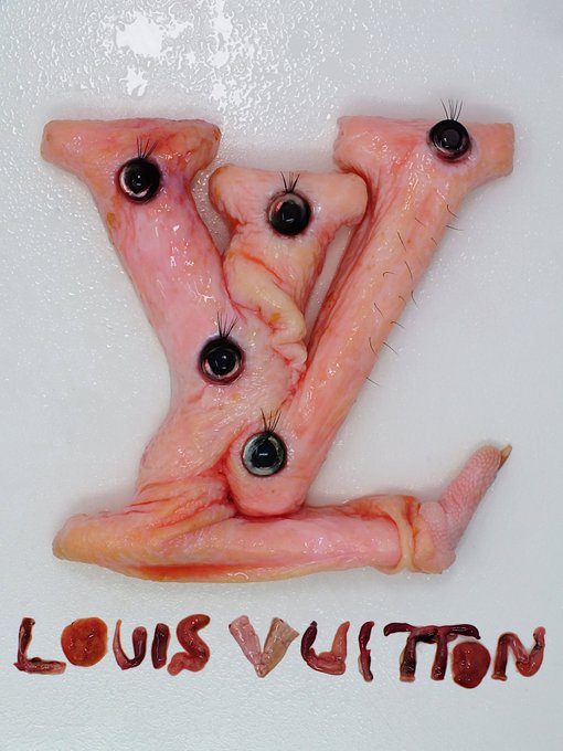 A macabre artistic creation spelling out the LV monogram and 'LOUIS VUITTON' using raw meat and animal parts with eyes, displayed on a white surface.