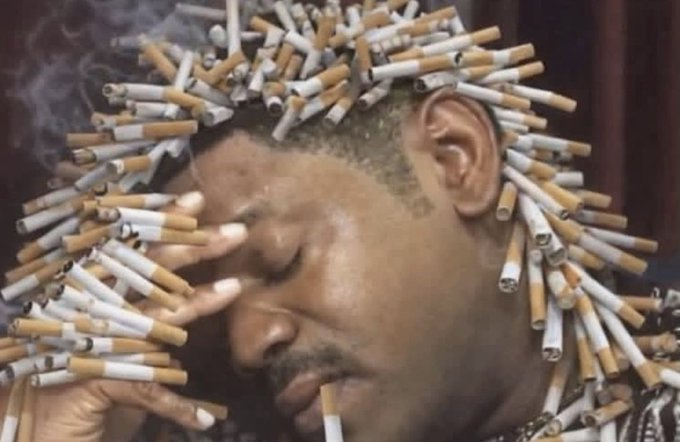 A close-up photo shows a man with numerous lit cigarettes arranged in his hair and on his face, with smoke rising and one cigarette dangling from his lips.