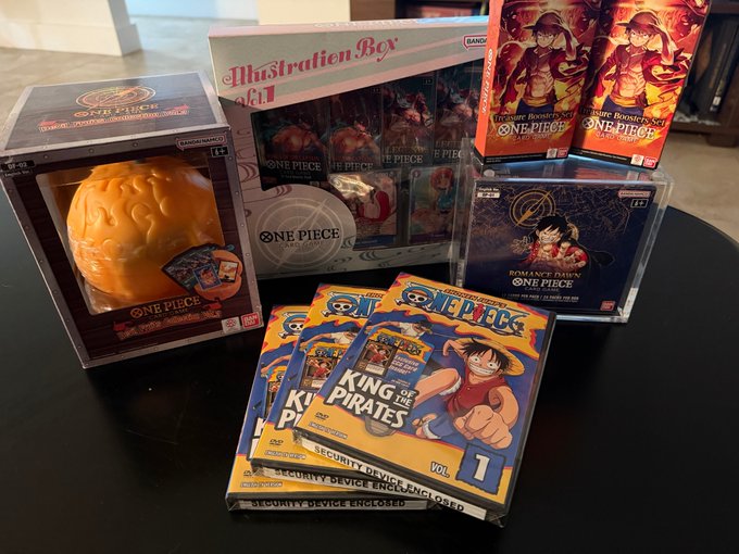 A collection of One Piece merchandise is displayed for sale, including a blue bottom figure with acrylic case (priced at $5,500), an Illustration Box Vol. 1 ($275), two "King of the Pirates" Vol. 1 DVD sets with promo cards ($200 each), and an Ace Devil Fruit figure, all matching the items listed in the trade post.