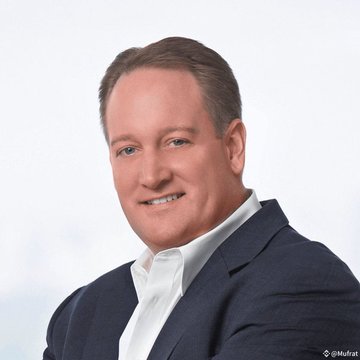 The image features a man wearing a suit, with his head turned towards the camera while smiling. He appears to be a successful individual or potentially an executive of a company. In the background behind him, there are text elements such as " valuation $500,000,000,000" and "more than 76,000 investors could be eligible". This suggests that Valhil Capital is seeking damages from over a hundred individuals who have invested in Ripple cryptocurrency, worth approximately US dollars, and has recently made a public statement.