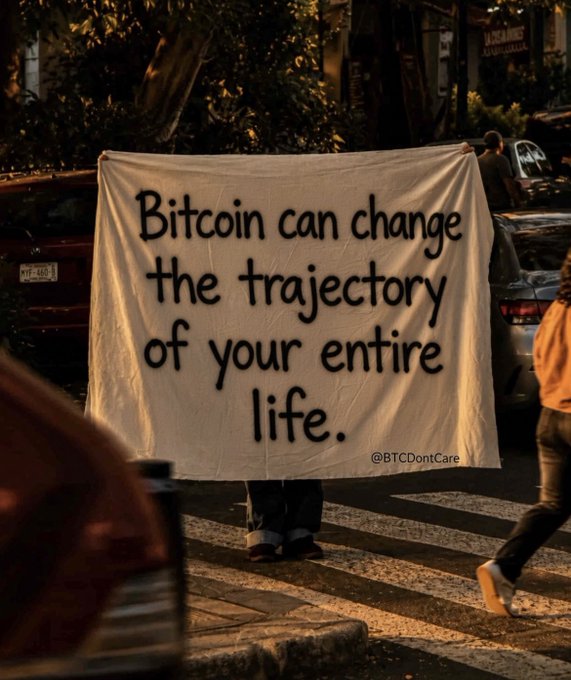 A person holding a banner on a street that reads, 'Bitcoin can change the trajectory of your entire life. @BTCDontCare'.