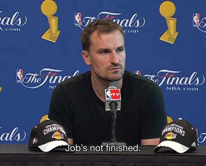 An NBA Finals press conference shows a man in a black shirt speaking into a microphone with championship hats in front of him, captioned 'Job's not finished.'
