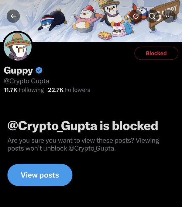 A Twitter/X profile page showing a blocked account '@Crypto_Gupta' (display name Guppy) with 11.7K Following and 22.7K Followers, featuring a banner with cartoon penguins and a 'Guppy' sign.