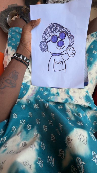 A hand holds a hand-drawn illustration of a character wearing a purple hat and sunglasses, with the name "Coby" written on its shirt, promoting the $coby meme coin as highlighted in the accompanying post.