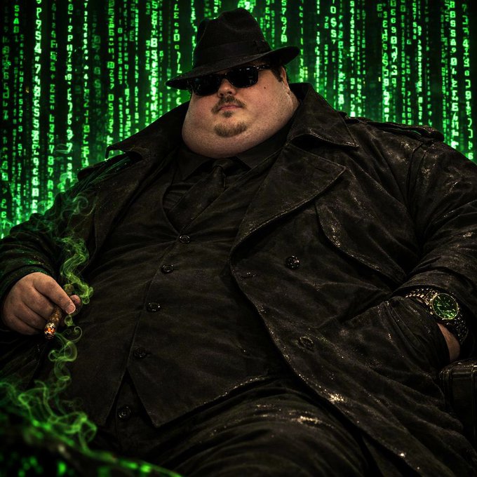 A portly figure in a black fedora, sunglasses, and trench coat smokes a cigar while seated in front of a cascading green Matrix-style code backdrop. The scene evokes a shady, wealth-peddling mastermind aesthetic—fitting for the post's theme of pitching the "$Memipede" as a "generational wealth opportunity" with a weekly vote.